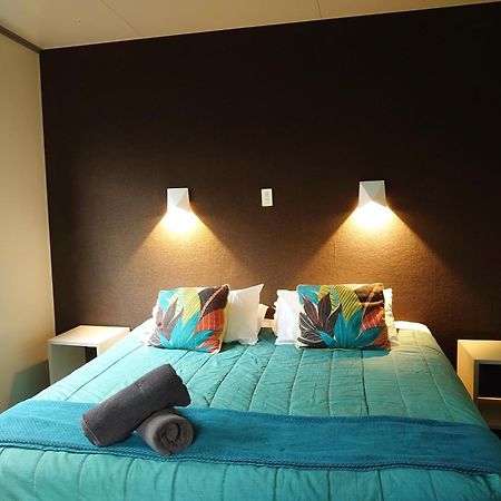 陶波德布雷思汽车旅馆酒店 外观 照片 The image shows a bedroom with a modern and inviting layout. The focal point is a bed with a vibrant turquoise comforter, decorated with two colorful pillows featuring floral patterns. On either side of the bed, there are small nightstands with wall-