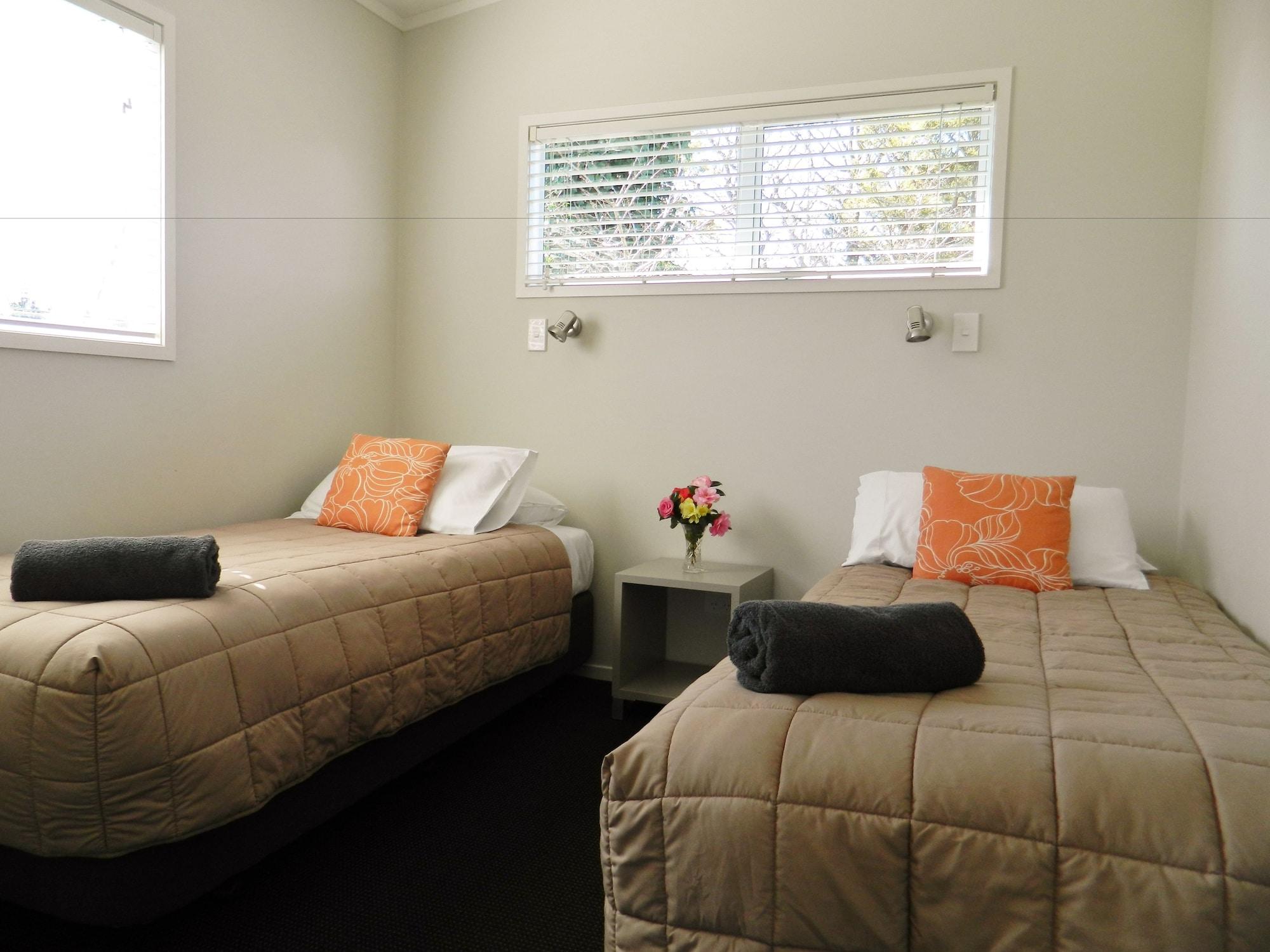 陶波德布雷思汽车旅馆酒店 外观 照片 The image shows a small, cozy room featuring two single beds. Each bed is dressed with a beige quilt and has an orange decorative pillow. There are two rolled towels placed on the beds. A small bedside table is located between the beds, with a vase o