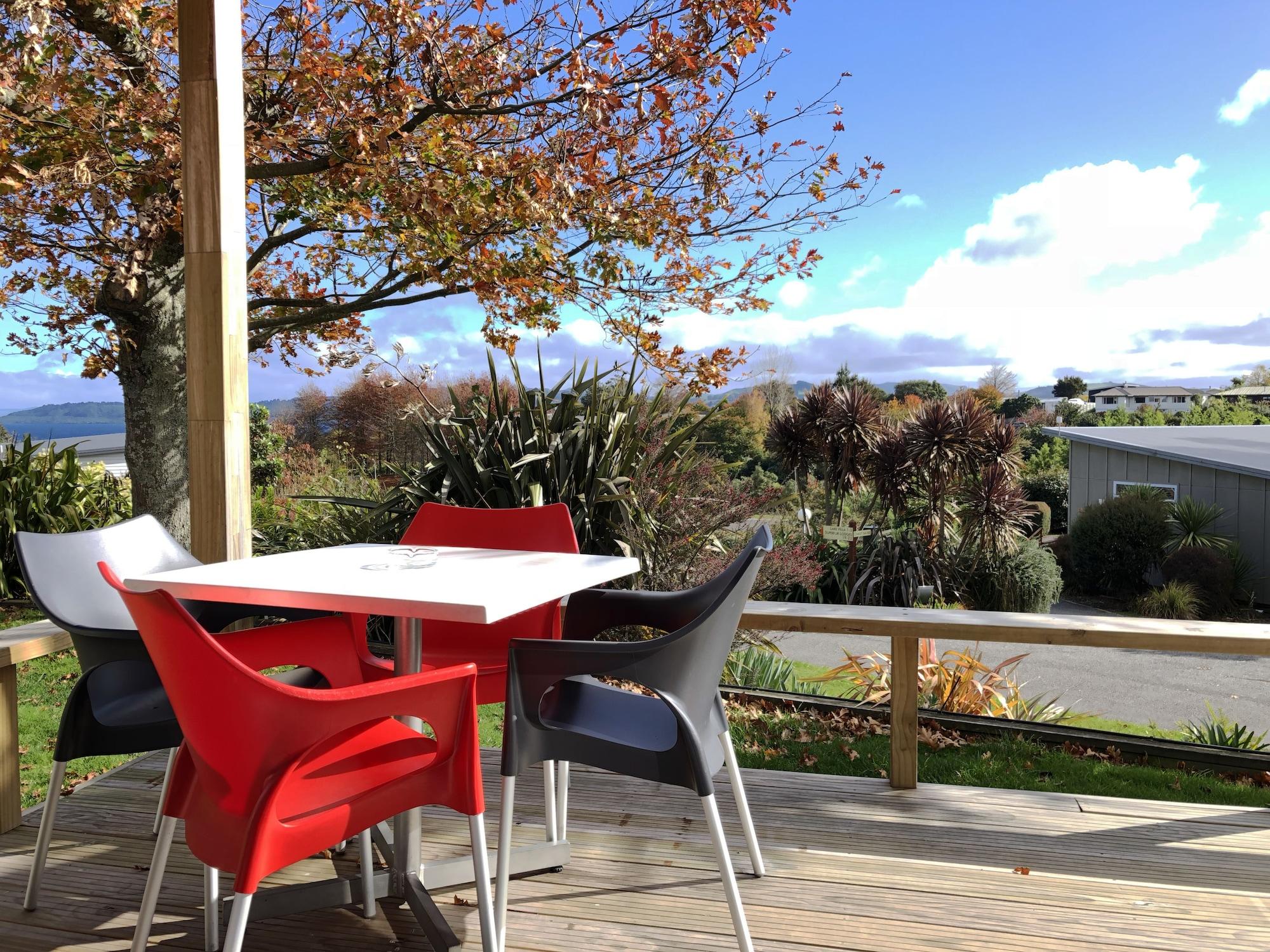 陶波德布雷思汽车旅馆酒店 外观 照片 The photo shows a picturesque outdoor seating area on a deck. There is a table surrounded by several chairs, with a couple of them in red and the others in gray and white. In the background, there are trees displaying autumn foliage, and beyond that,