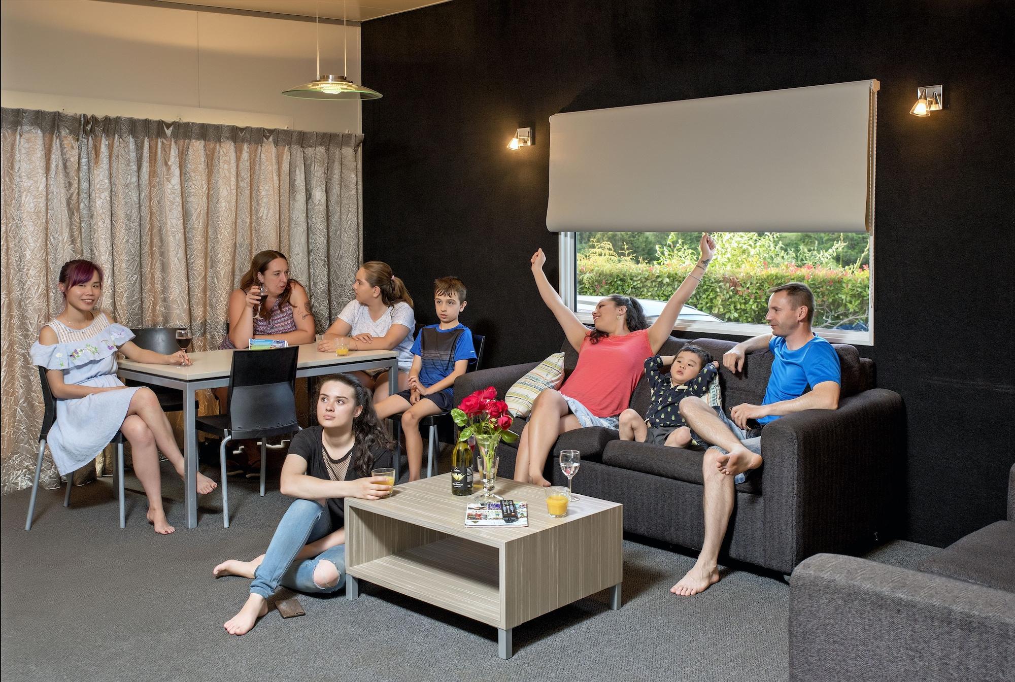 陶波德布雷思汽车旅馆酒店 外观 照片 The photo shows a group of people gathered in a cozy living room. There are several adults and children interacting with each other. One woman in a red top appears to be celebrating or expressing excitement, while others are engaged in conversation o