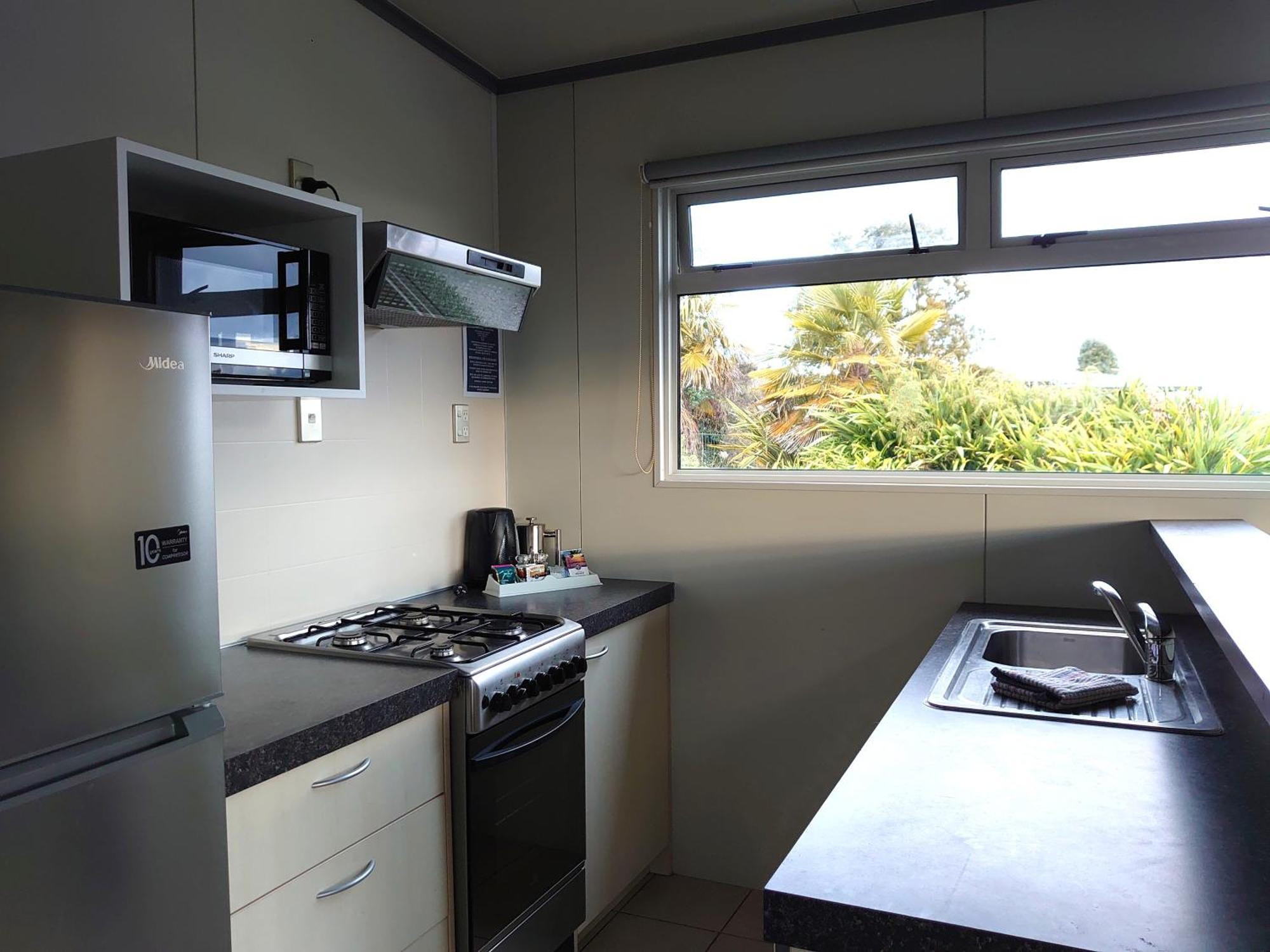 陶波德布雷思汽车旅馆酒店 外观 照片 The photo shows a kitchen equipped with modern appliances. On the left side, there is a refrigerator and a microwave above it. The kitchen features a gas stove with a range hood above. To the right, there is a kitchen sink with a countertop. A window