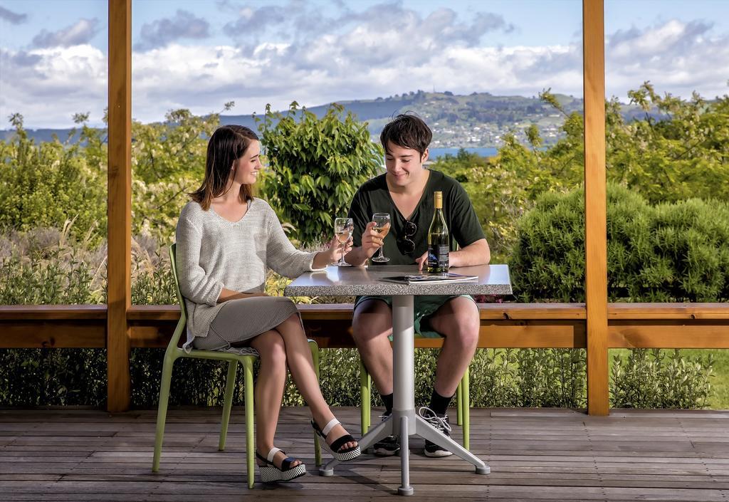 陶波德布雷思汽车旅馆酒店 外观 照片 The photo shows a young couple sitting at a table outdoors. They are enjoying drinks, with the woman wearing a light-colored sweater and a skirt, while the man is dressed in a dark shirt and shorts. The table is set with two glasses and a bottle of w