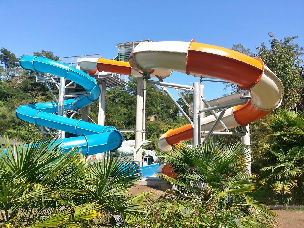 陶波德布雷思汽车旅馆酒店 外观 照片 The photo shows a water park featuring two large water slides. One slide is blue and curves gracefully, while the other is orange and white, twisting as it descends. They are supported by a metal structure and surrounded by lush greenery, including p