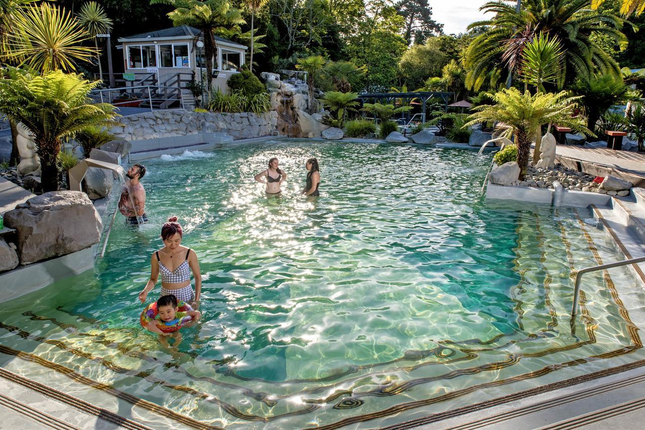 陶波德布雷思汽车旅馆酒店 外观 照片 The photo shows a scenic outdoor swimming pool surrounded by lush greenery, including palm trees. In the pool, several people are enjoying the water, with one woman holding a child who is in a flotation device. The atmosphere appears relaxed and invi