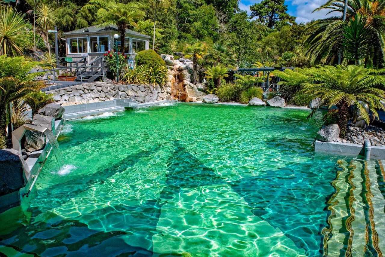 陶波德布雷思汽车旅馆酒店 外观 照片 The photo showcases a vibrant, natural-looking pool with crystal-clear, turquoise water. Surrounding the pool are lush green plants and palm trees, creating a tropical atmosphere. In the background, there is a white building, possibly a facility or a